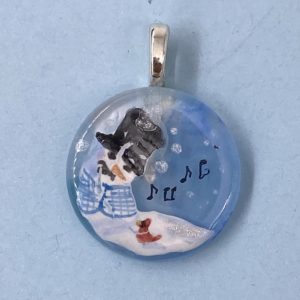 1" glass circle pendant with a snow person in a black top hat and blue checked vest singing to a red cardinal at it's base