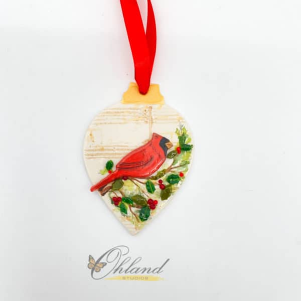 drop shaped ornament with faded music in the background and a bright red cardinal sitting on a holly bush branch