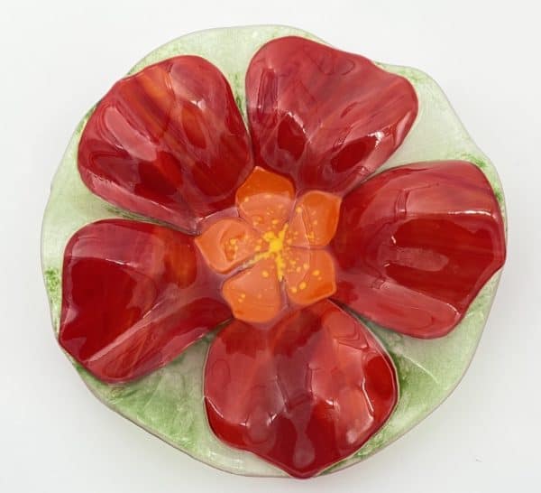 red five petal flower on a 7.5" across bowl, the flower has an orange center with yellow flecks and is on a transparent green background, the bowl is an irregular organic waving shape