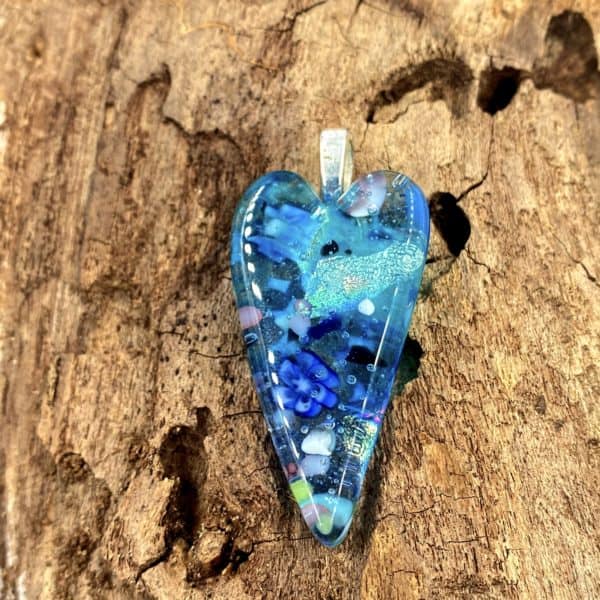 Narrow glass heart pendant with translucent teal glass and bits of turquoise opaque, cobalt and white glass throughout, pendant has a silver bail