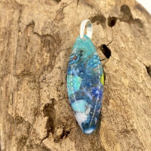 this is a pointed oval pendant that is translucent and has a main color of dark turquoise with bits of cobalt, light turquoise, white and green throughout, it has a silver bail