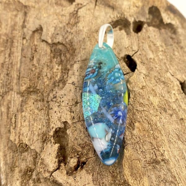 this is a pointed oval pendant that is translucent and has a main color of dark turquoise with bits of cobalt, light turquoise, white and green throughout, it has a silver bail