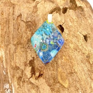This is a multi colored pendant in blues and greens with sparkly bits and tiny flowers. It is shaped like a diamond and has a sterling silver bail.