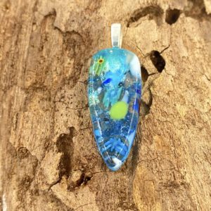 Photo of pendant which is a long tear drop with the point at the bottom, the pendant is blue and teal translucent glass with bits of shiny blue/green and specks of bright green and white