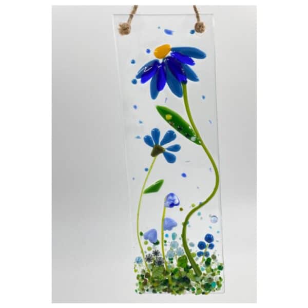 close up of a blue corn flower sun catcher with a small bud and several small blue flowers at the bottom with green stems and grass