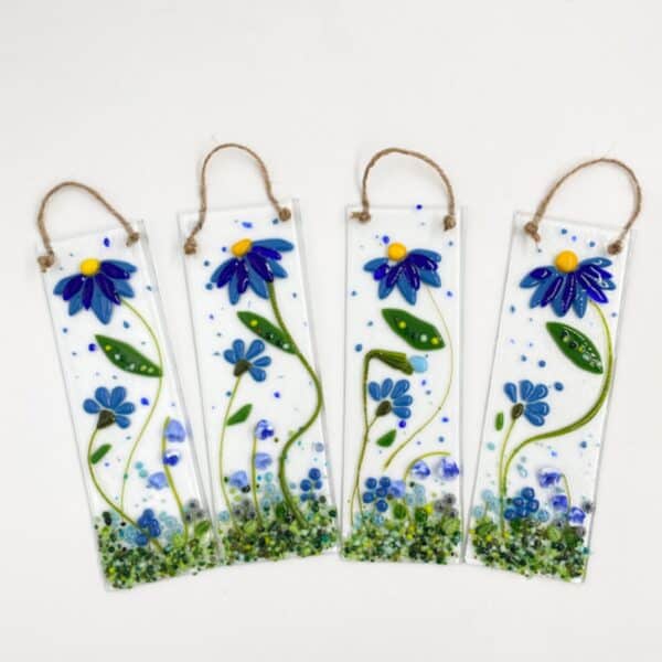 four sun catchers with a main blue flower with yellow center, blue bud and green bottom with small blue flowers. the sun catcher has a jute string attached for hanging